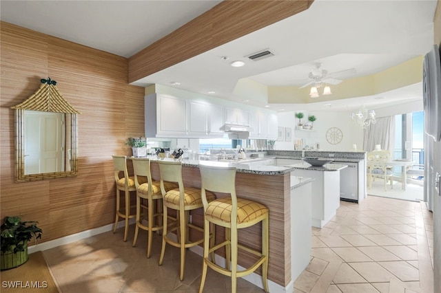 kitchen with kitchen peninsula, light stone countertops, light tile patterned floors, white cabinets, and a kitchen breakfast bar