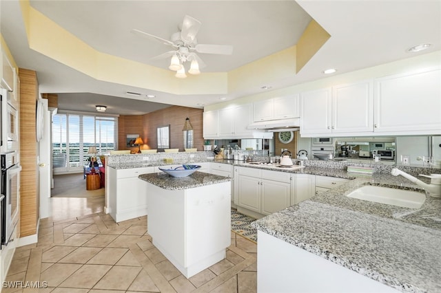 kitchen featuring kitchen peninsula, a kitchen island, and light stone counters