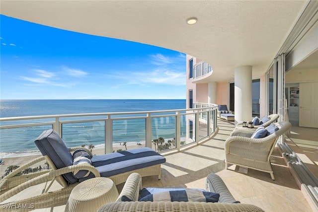 balcony with an outdoor living space, a water view, and a view of the beach