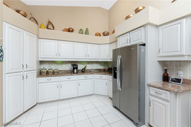 kitchen featuring stainless steel refrigerator with ice dispenser, dark stone counters, light tile patterned floors, and white cabinets