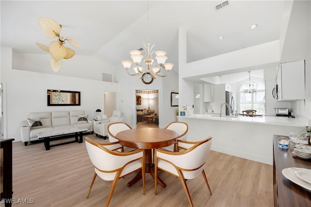 dining area with lofted ceiling, light wood-style floors, visible vents, and ceiling fan with notable chandelier