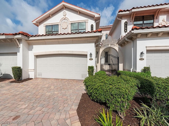 mediterranean / spanish-style house featuring decorative driveway, a gate, and stucco siding