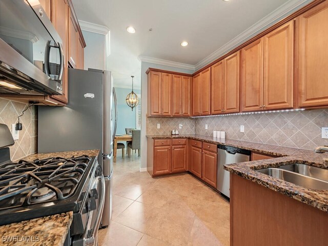 kitchen with a sink, appliances with stainless steel finishes, dark stone counters, brown cabinetry, and crown molding