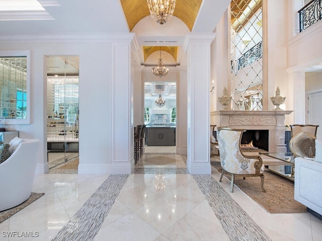233 Mermaids Bight, Naples, FL 34103 - entryway featuring crown molding, decorative columns, a fireplace, a decorative wall, and a notable chandelier