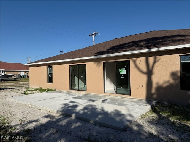back of property with a patio area, roof with shingles, and stucco siding