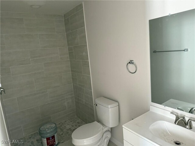 bathroom with toilet, a tile shower, and vanity