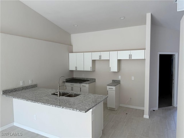 kitchen featuring a peninsula, a sink, light stone countertops, and white cabinets