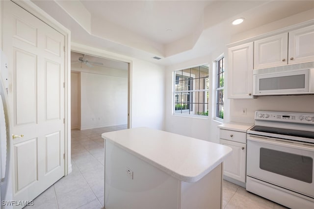 kitchen with white appliances, white cabinets, a raised ceiling, a center island, and light countertops