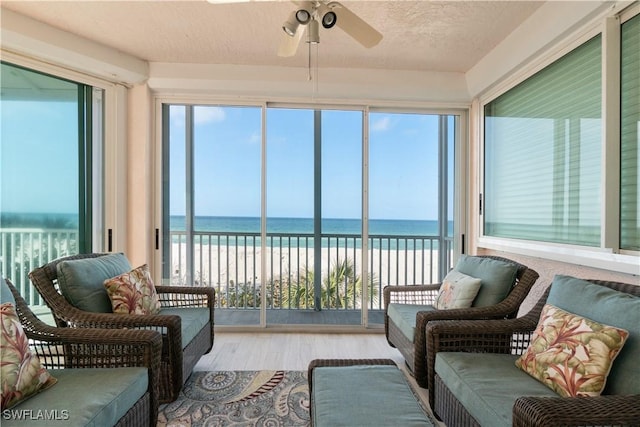 sunroom / solarium featuring a ceiling fan, a water view, and a beach view