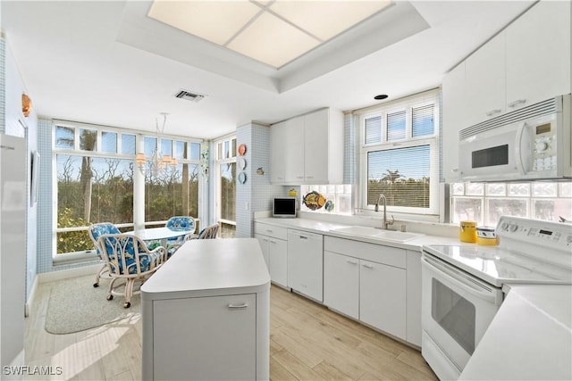 kitchen with white appliances, decorative light fixtures, light countertops, white cabinetry, and a sink