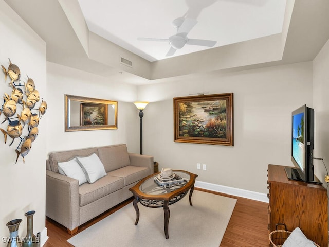 living room featuring wood-type flooring, ceiling fan, and a tray ceiling