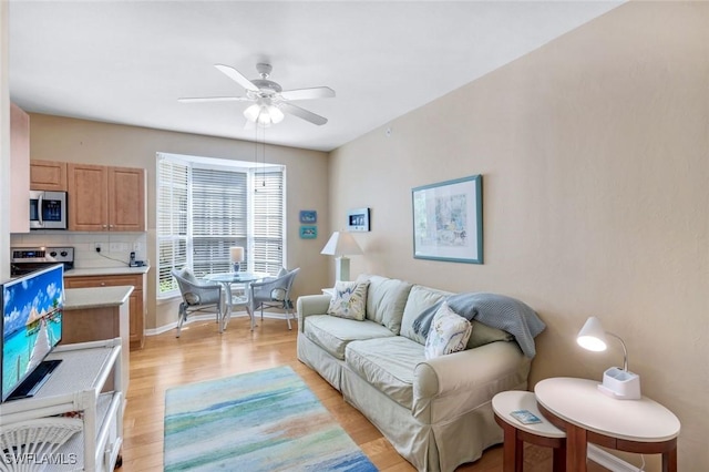 living area featuring baseboards, a ceiling fan, and light wood finished floors