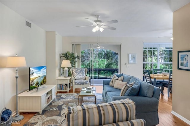 living room featuring ceiling fan, visible vents, baseboards, and wood finished floors