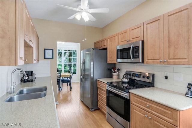 kitchen featuring tasteful backsplash, light wood-style floors, stainless steel appliances, a ceiling fan, and a sink