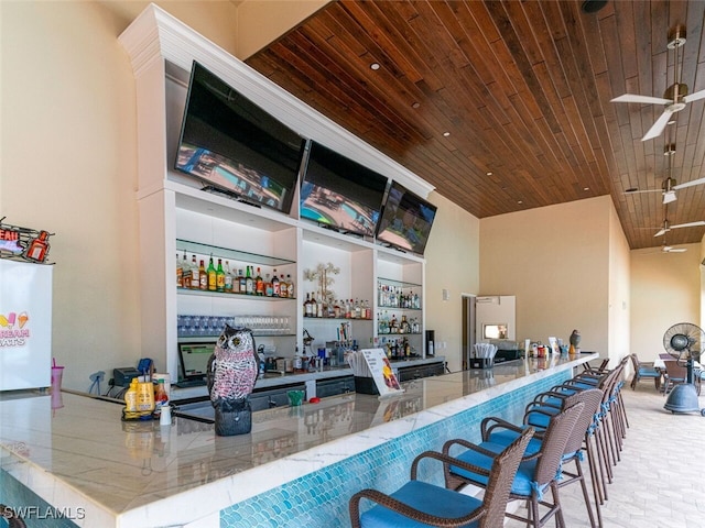 bar featuring a community bar, wood ceiling, a towering ceiling, and ceiling fan