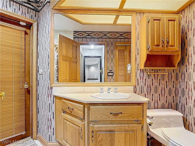 bathroom with vanity, toilet, and wallpapered walls