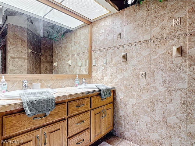 full bath featuring double vanity, tiled shower, a sink, and tile walls