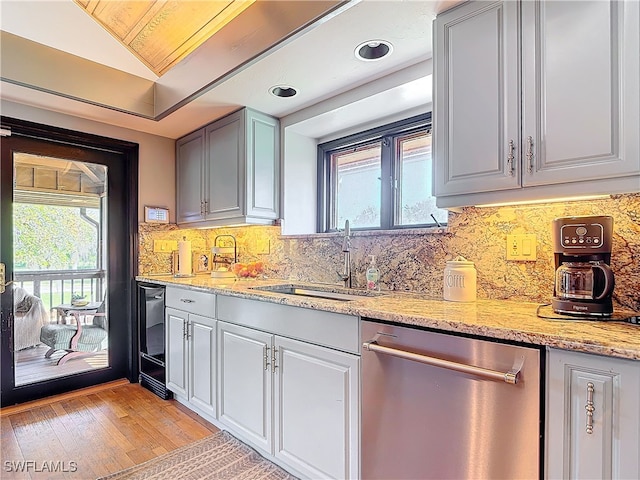 kitchen featuring a sink, stainless steel dishwasher, backsplash, light stone countertops, and light wood finished floors