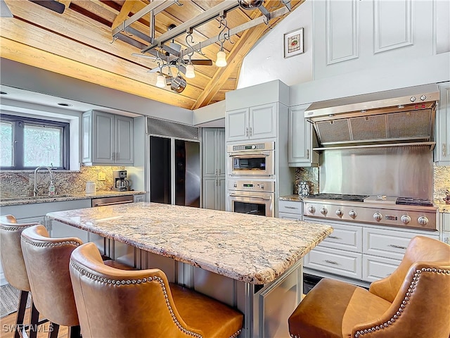 kitchen with range hood, tasteful backsplash, lofted ceiling with beams, appliances with stainless steel finishes, and a kitchen island