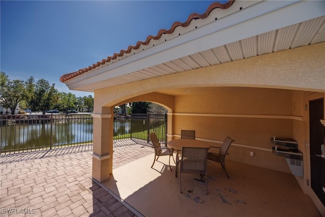 view of patio with outdoor dining space, fence, and a water view