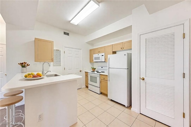 kitchen with white appliances, a peninsula, a sink, light brown cabinetry, and a kitchen breakfast bar