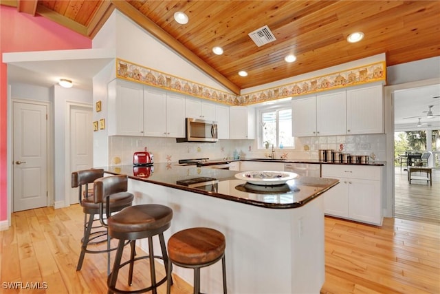 kitchen featuring lofted ceiling, white cabinets, a kitchen bar, kitchen peninsula, and stainless steel appliances