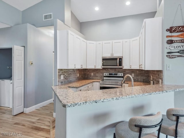 kitchen featuring a peninsula, visible vents, light stone counters, and stainless steel appliances