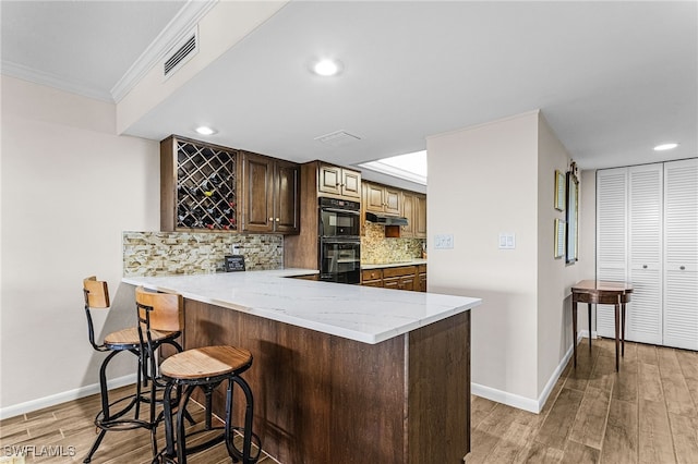 kitchen with a breakfast bar, tasteful backsplash, visible vents, dobule oven black, and a peninsula