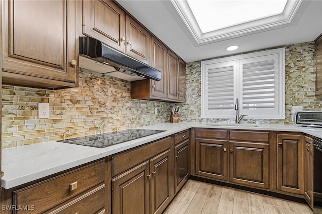 kitchen featuring under cabinet range hood, light countertops, light wood-type flooring, backsplash, and black appliances