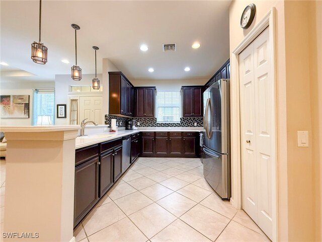 kitchen featuring dark brown cabinetry, a peninsula, a sink, stainless steel appliances, and backsplash