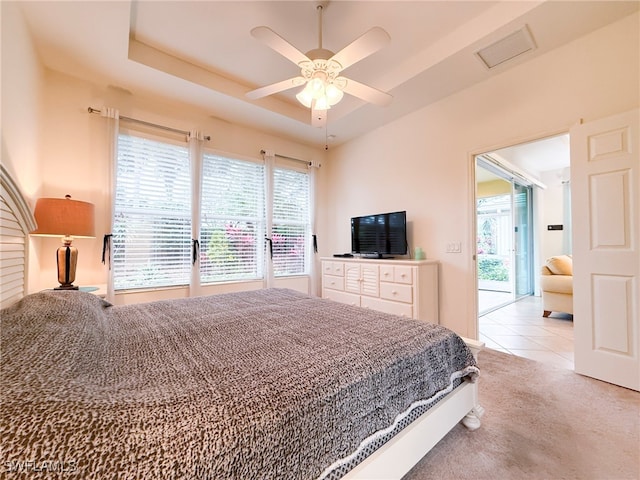 carpeted bedroom with visible vents, ceiling fan, access to exterior, tile patterned flooring, and a tray ceiling