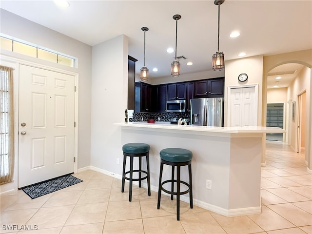 kitchen with arched walkways, a breakfast bar area, light tile patterned flooring, stainless steel appliances, and light countertops