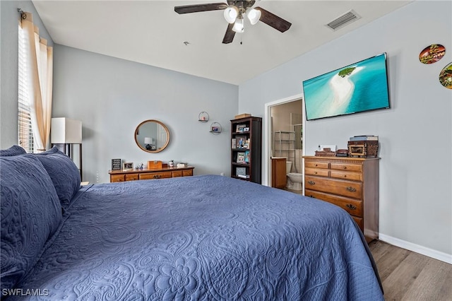 bedroom with wood finished floors, a ceiling fan, visible vents, baseboards, and ensuite bath