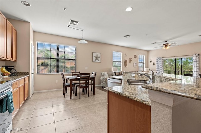 kitchen with brown cabinetry, a sink, dishwashing machine, and light tile patterned floors