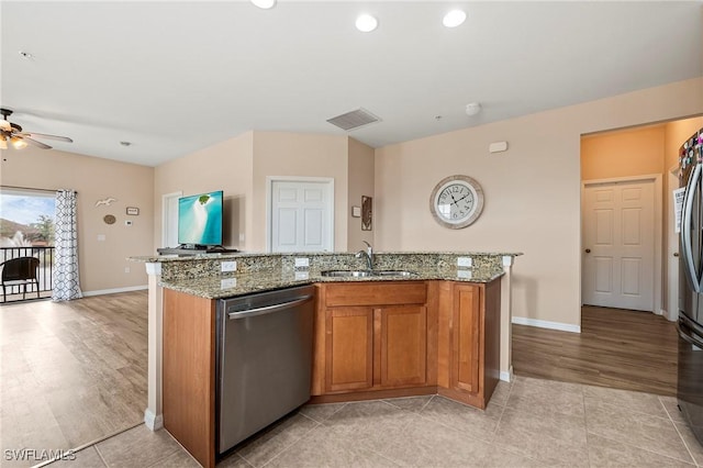 kitchen with brown cabinets, stainless steel dishwasher, a sink, an island with sink, and light stone countertops