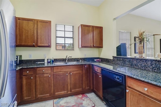 kitchen with black dishwasher, dark stone countertops, a sink, and freestanding refrigerator