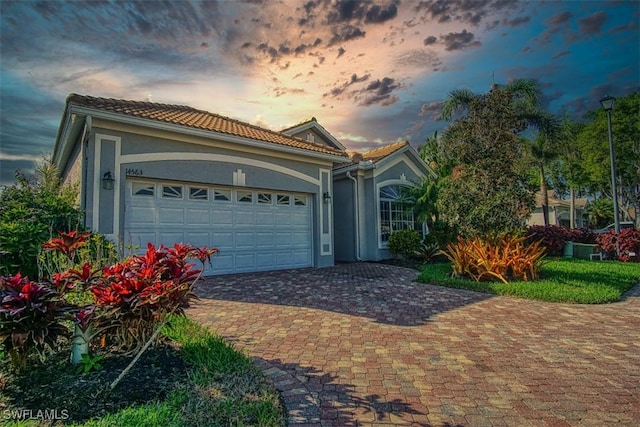 view of front of house with an attached garage, a tiled roof, decorative driveway, and stucco siding