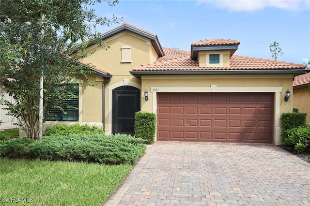 mediterranean / spanish home featuring a garage, decorative driveway, a tiled roof, and stucco siding