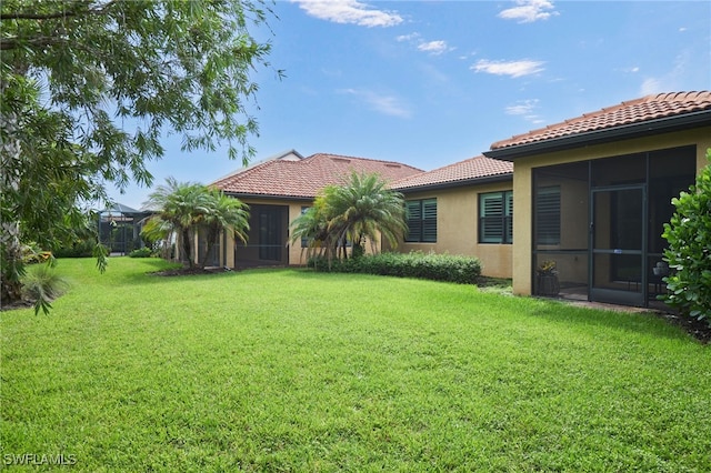 rear view of house featuring stucco siding, a tile roof, glass enclosure, and a yard