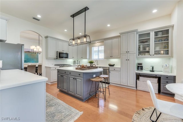 kitchen with arched walkways, gray cabinetry, a breakfast bar, appliances with stainless steel finishes, and a center island