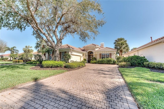 mediterranean / spanish-style house with decorative driveway, a chimney, a front yard, a garage, and a tiled roof