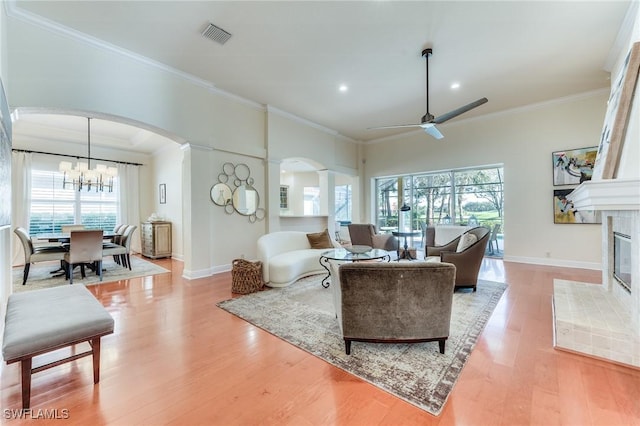 living area with arched walkways, crown molding, a fireplace, light wood-style floors, and baseboards