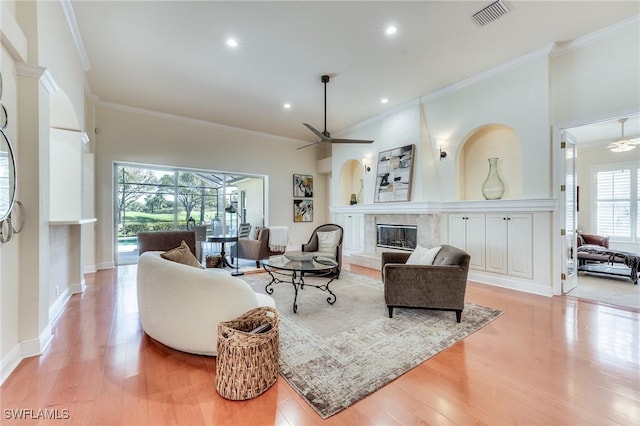 living area with ceiling fan, a premium fireplace, visible vents, ornamental molding, and light wood finished floors