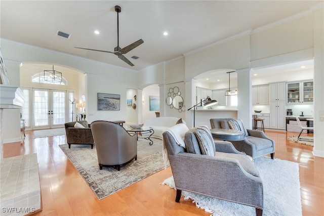 living area with light wood-type flooring, arched walkways, crown molding, and french doors