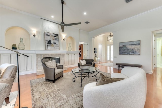 living room with arched walkways, visible vents, light wood-style flooring, crown molding, and a fireplace