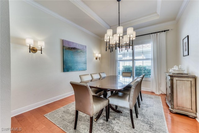 dining area with a notable chandelier, baseboards, light wood-type flooring, a raised ceiling, and crown molding