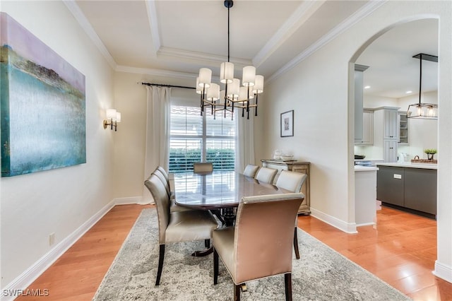 dining area with arched walkways, a raised ceiling, crown molding, and light wood finished floors