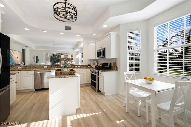 kitchen with appliances with stainless steel finishes, white cabinetry, a tray ceiling, a kitchen island, and kitchen peninsula