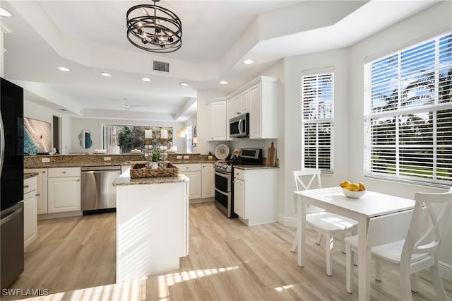 kitchen with a raised ceiling, stainless steel appliances, light wood-style floors, and visible vents