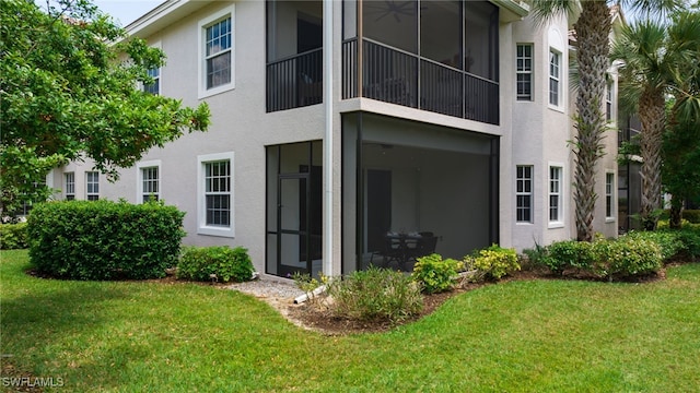 back of house with a sunroom, stucco siding, and a lawn